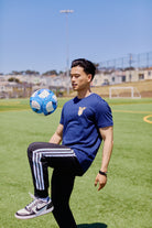 Wearing the WC x SFP Tee, a man balances a blue and white soccer ball on his knee in sunny San Francisco, channeling Team USA’s energy as he trains for the World Cup.