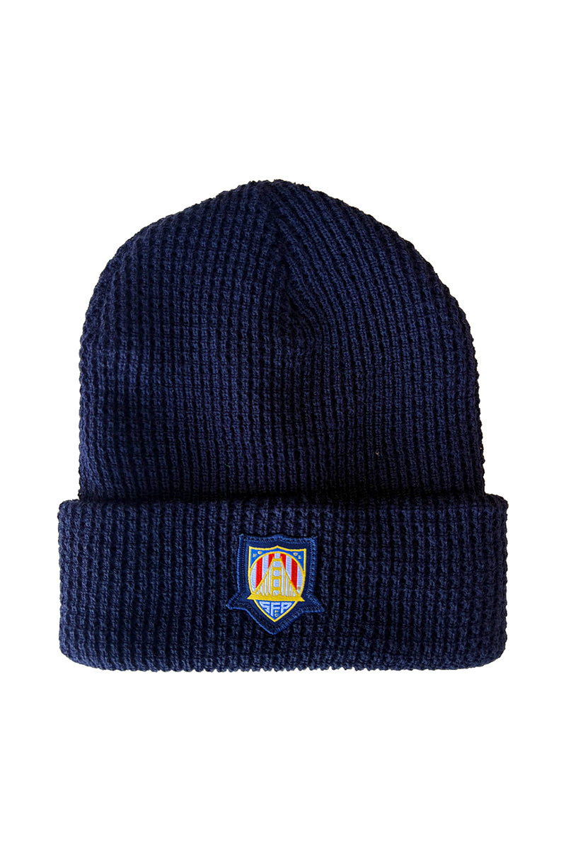The WC x SFP Beanie is a navy blue knit hat with a folded brim and a vibrant embroidered crest, inspired by SFP beanies worn by US Men's National Team fans.