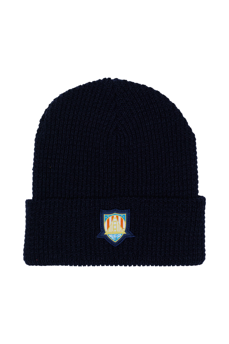 The WC x SFP Beanie is a black knit hat featuring a colorful embroidered shield logo on the folded brim, inspired by the US Men's National Team.