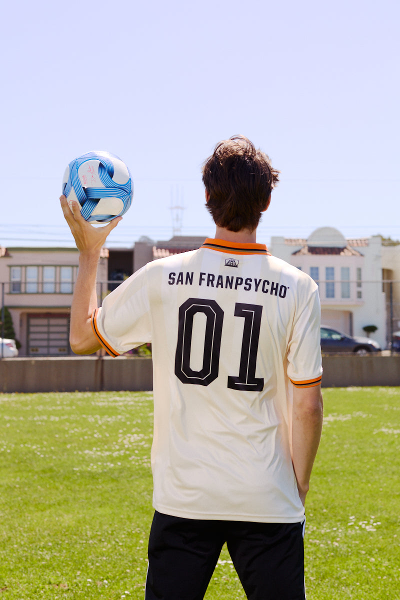 Person holding a blue and white soccer ball, wearing the WC x SFP Jersey - Away inspired by the US Men's National Team, standing on grass.