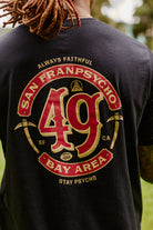 Wearing the Niners Faithful Tee, a black unisex t-shirt featuring San Franpsycho 49 Bay Area and graphic elements on the back—perfect for any fan representing San Francisco.