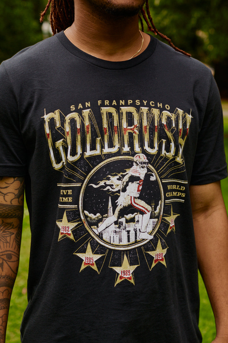 A man wearing the Gold Rush Tee - Vintage Black, featuring a football graphic and championship years, celebrates the spirit of San Francisco.