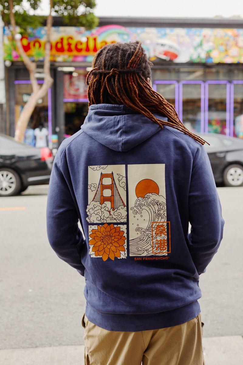 A person with dreadlocks wears the Sunset Dahlia Pullover Hoodie, a vintage mineral wash hoodie adorned with Japanese art-inspired graphics of the Golden Gate Bridge, waves, sun, and a flower—echoing the design found on the Sunset Dahlia Tee.