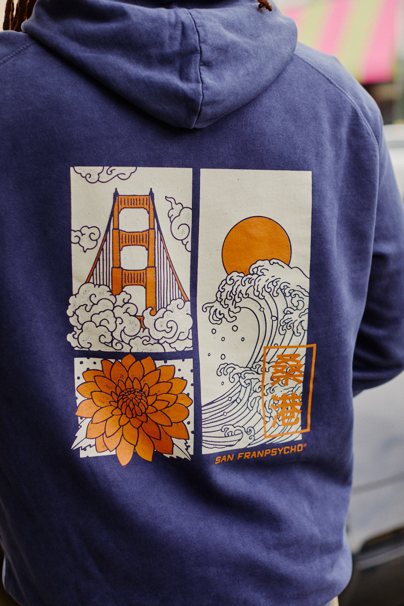 Wearing the Sunset Dahlia Pullover Hoodie featuring hand-printed artwork of a bridge, flower, waves, and the sun on the back—crafted in San Francisco for an authentic touch.