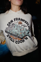 Cream-colored Still Cookin’ Crop Hoodie featuring a graphic with the text San Franpsycho Still Cookn.