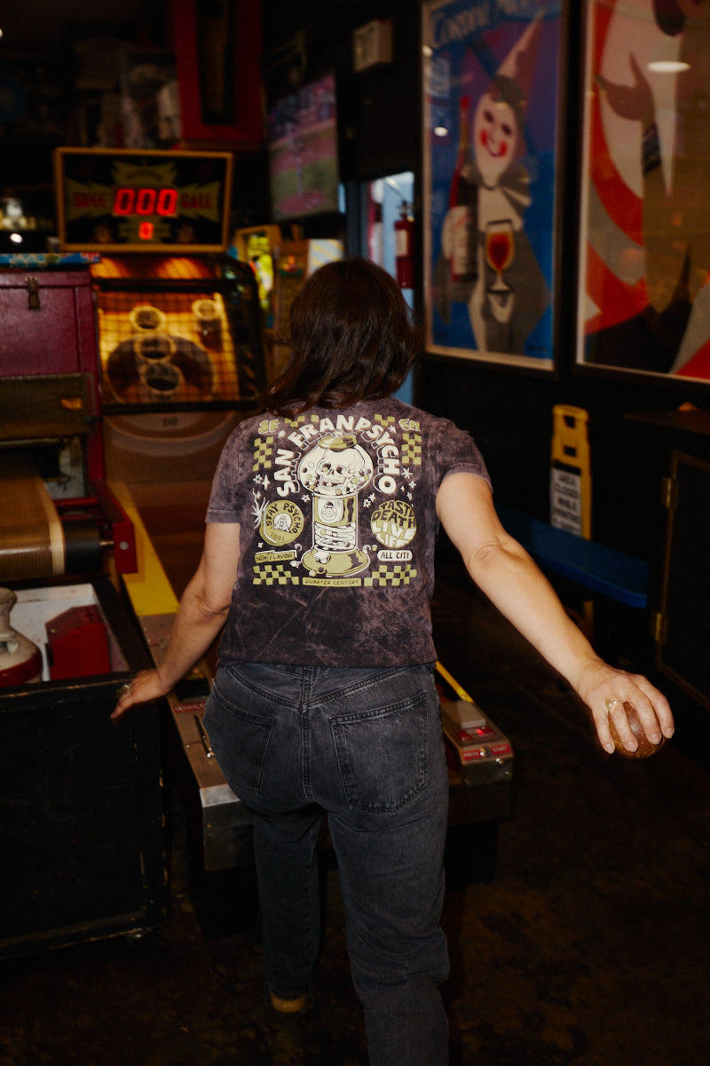 A person wearing a gray Quarter Cent Tee plays a game of skee-ball in an arcade.