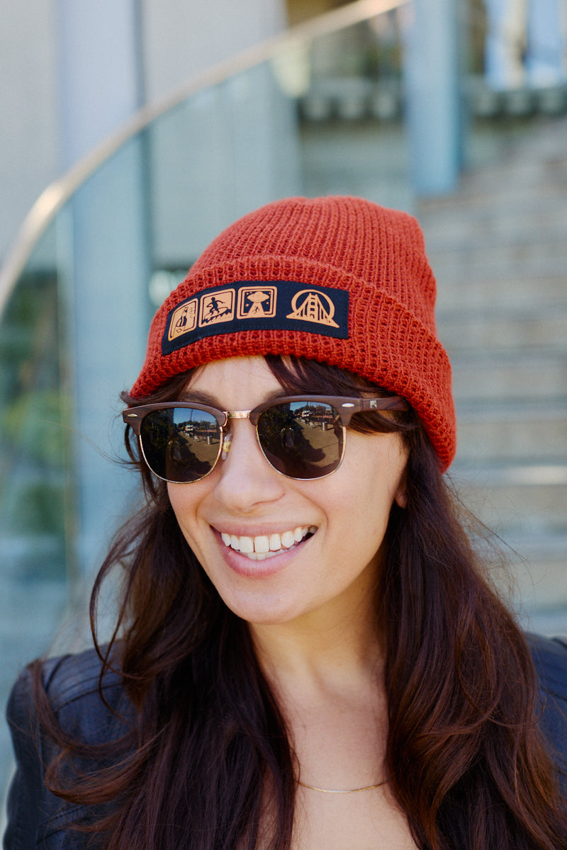 A rust-colored Icons Beanie with a ribbed texture and a patch featuring beer and surf icons.