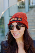 A rust-colored Icons Beanie with a ribbed texture and a patch featuring beer and surf icons.