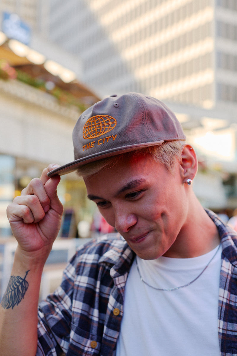 The City Hat, a grey snapback embroidered with an orange globe icon and the words THE CITY.
