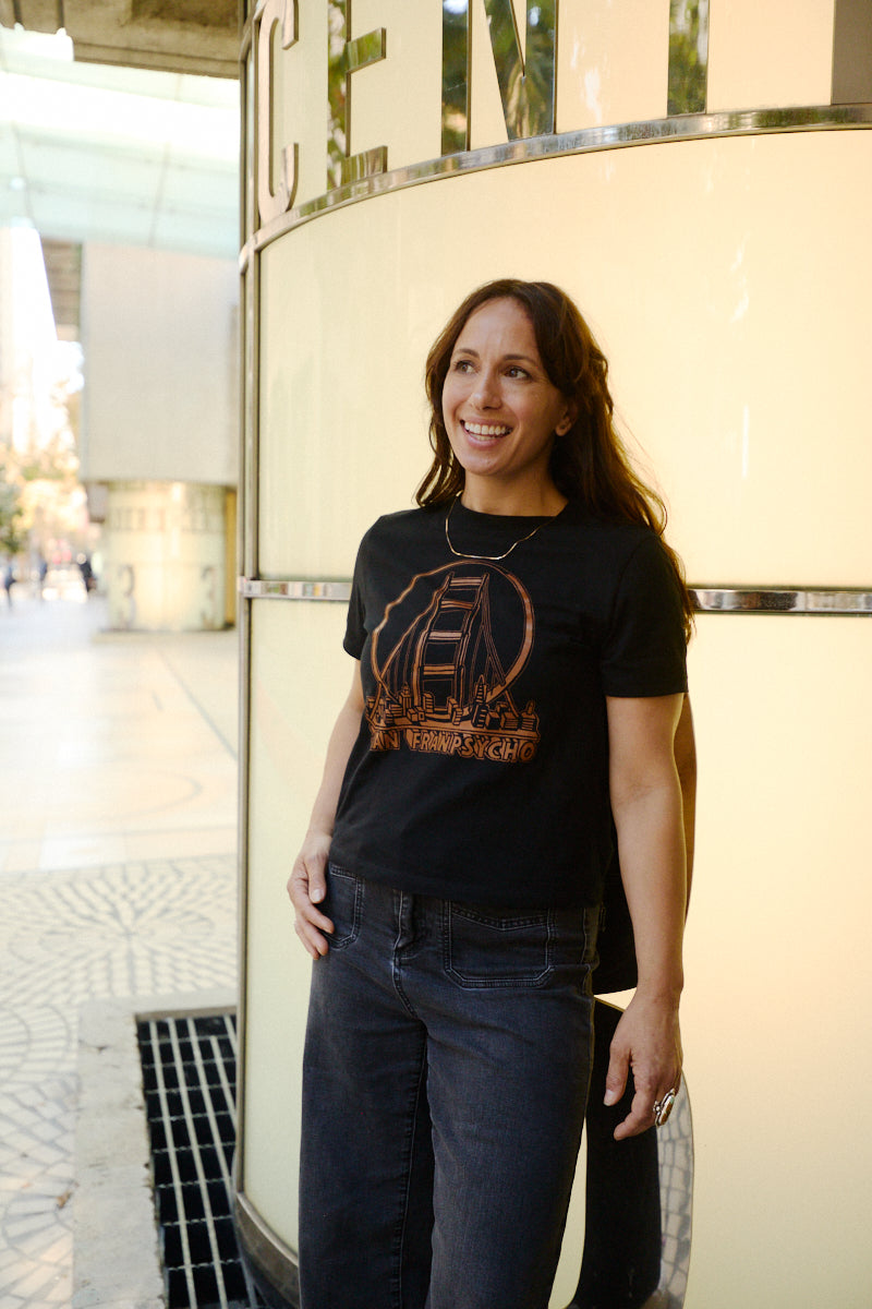A woman wears a Women’s 3D Logo Tee, a boxy crop top featuring the Golden Gate Bridge and San Franpsycho text.