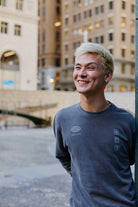 Smiling person wearing a charcoal 3D Logo Crewneck sweatshirt with a graphic logo.