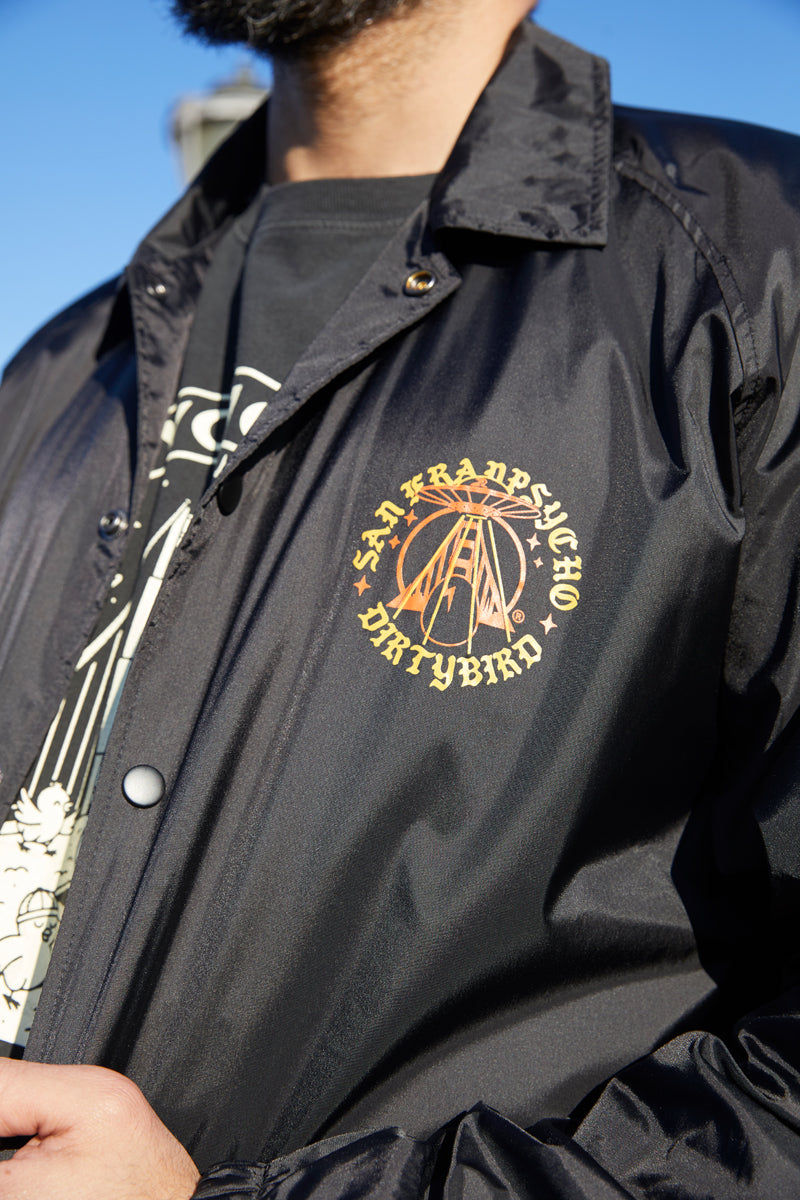 A person wears the Dirty UFO Coaches Jacket in black, showcasing a yellow San Francisco Dirtybird logo on the chest—a standout Bay Area streetwear piece.