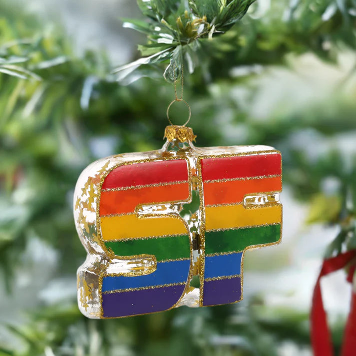 The locally crafted Xmas Ornaments by Local Elves, featuring the iconic rainbow-colored SF, hang beautifully on a Christmas tree branch, perfectly capturing the essence of San Francisco.