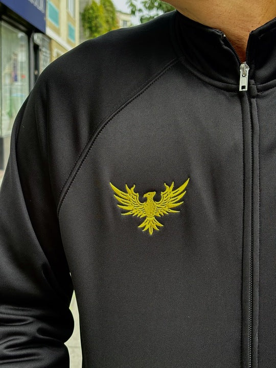 A person wearing the WC x SFP Zip-Up Jacket, featuring a yellow phoenix emblem on the chest.