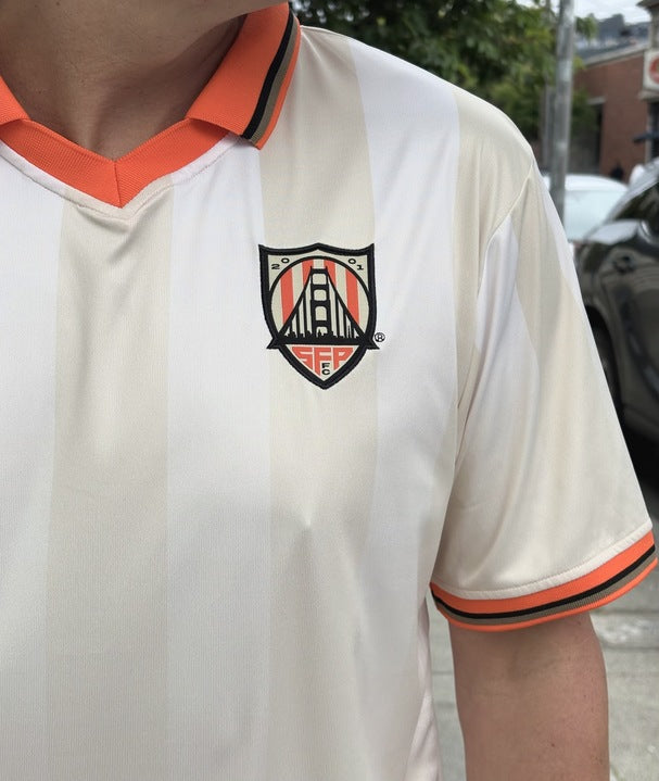 Person wearing the WC x SFP Jersey - Away, a white and orange fan fit jersey featuring a crest with a bridge and the initials SF.