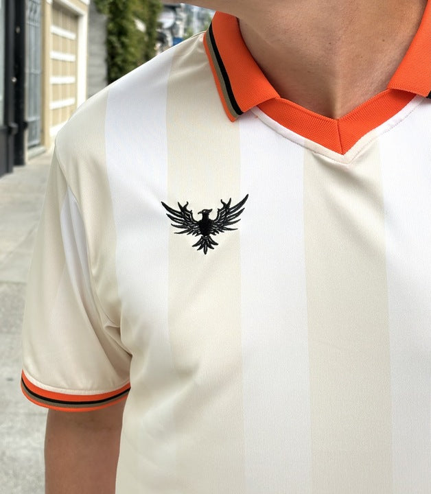 Person wearing the WC x SFP Jersey - Away, featuring a cream design, orange collar, and eagle emblem on the left chest.