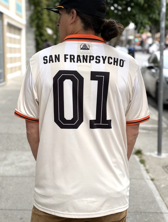 Person wearing a WC x SFP Jersey - Away, standing on a city sidewalk lined with trees and parked cars.