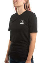 A person is wearing a Black & Orange Street Skull Tee crafted from soft Airlume cotton, featuring a small logo on the left side, while standing against a white background.