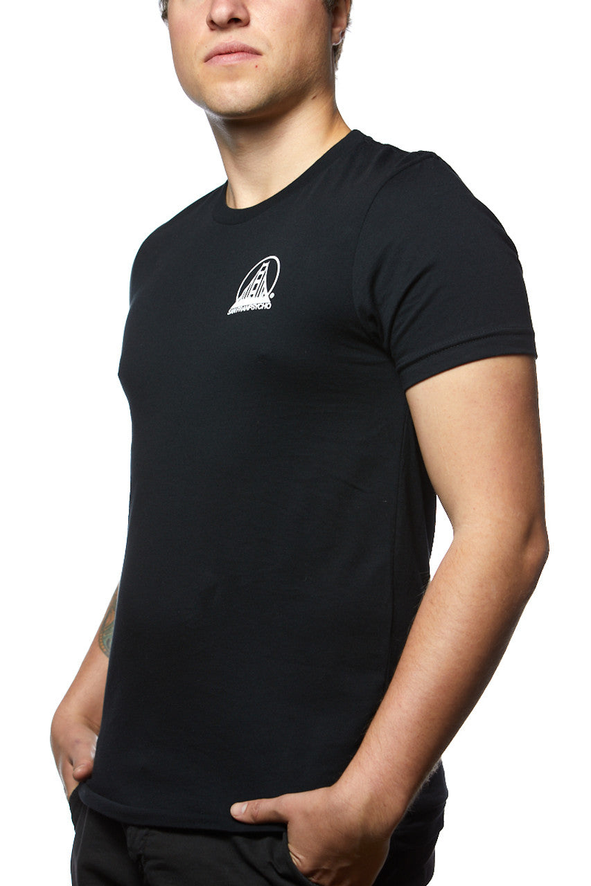 A person in a Black & Orange Street Skull Tee, crafted from soft Airlume cotton, featuring a small white logo on the chest, standing with hands in pockets.