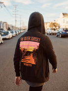 A person strolls down Noriega St, sporting the Outer Sunset Zip-Up Hoodie with a vibrant sunset graphic and "The Outer Sunset, San Francisco" text.