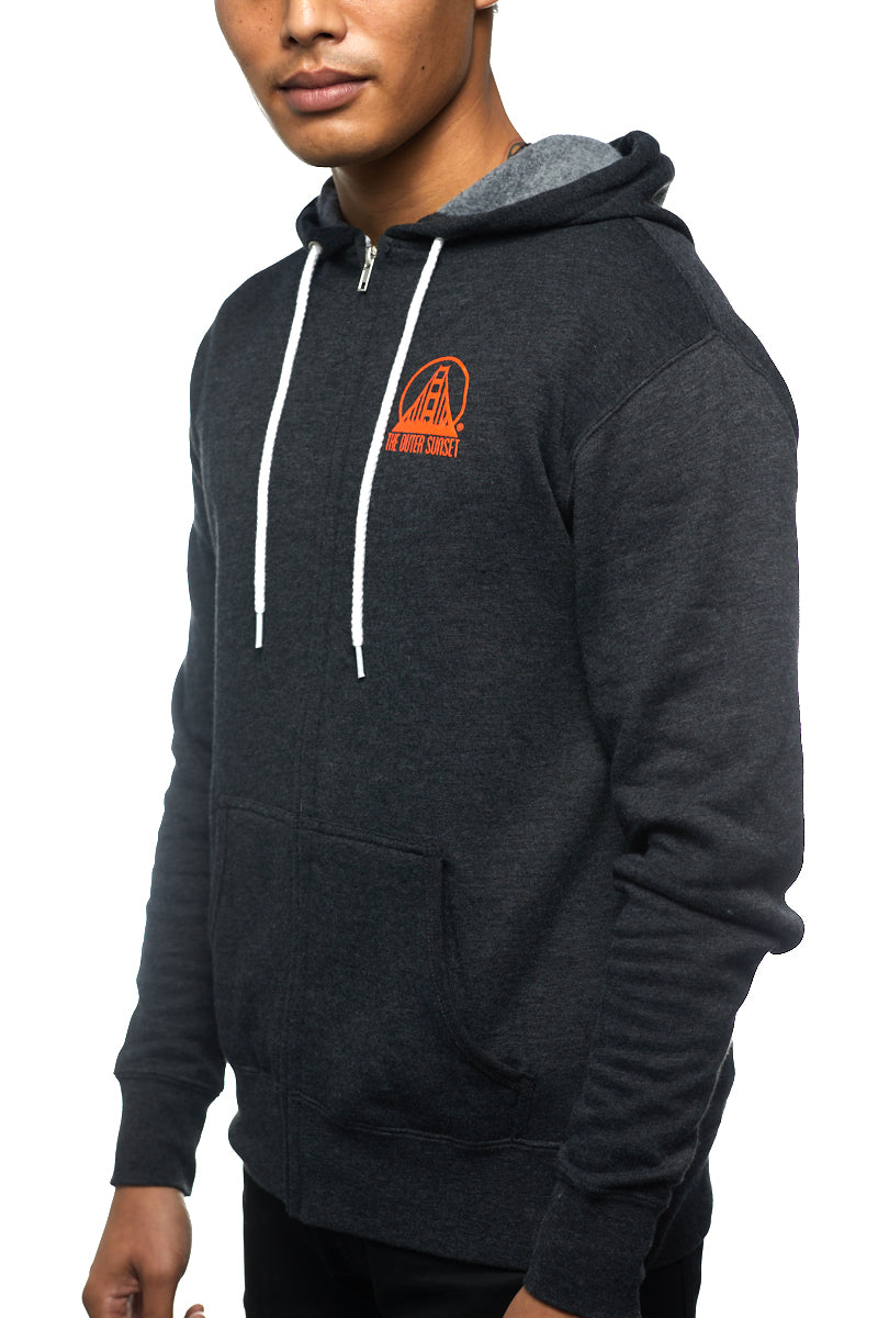 Wearing the Outer Sunset Zip-Up Hoodie, featuring a dark design with an orange logo and white drawstrings, a person stands against a white backdrop, perfectly capturing its laid-back vibe.