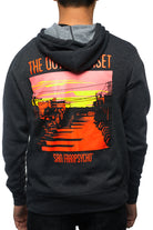 A person wearing the Outer Sunset Zip-Up Hoodie, featuring a vibrant sunset graphic and the text "The Outer Sunset San Franpsycho," strolls down Noriega St, capturing the essence of this iconic neighborhood.
