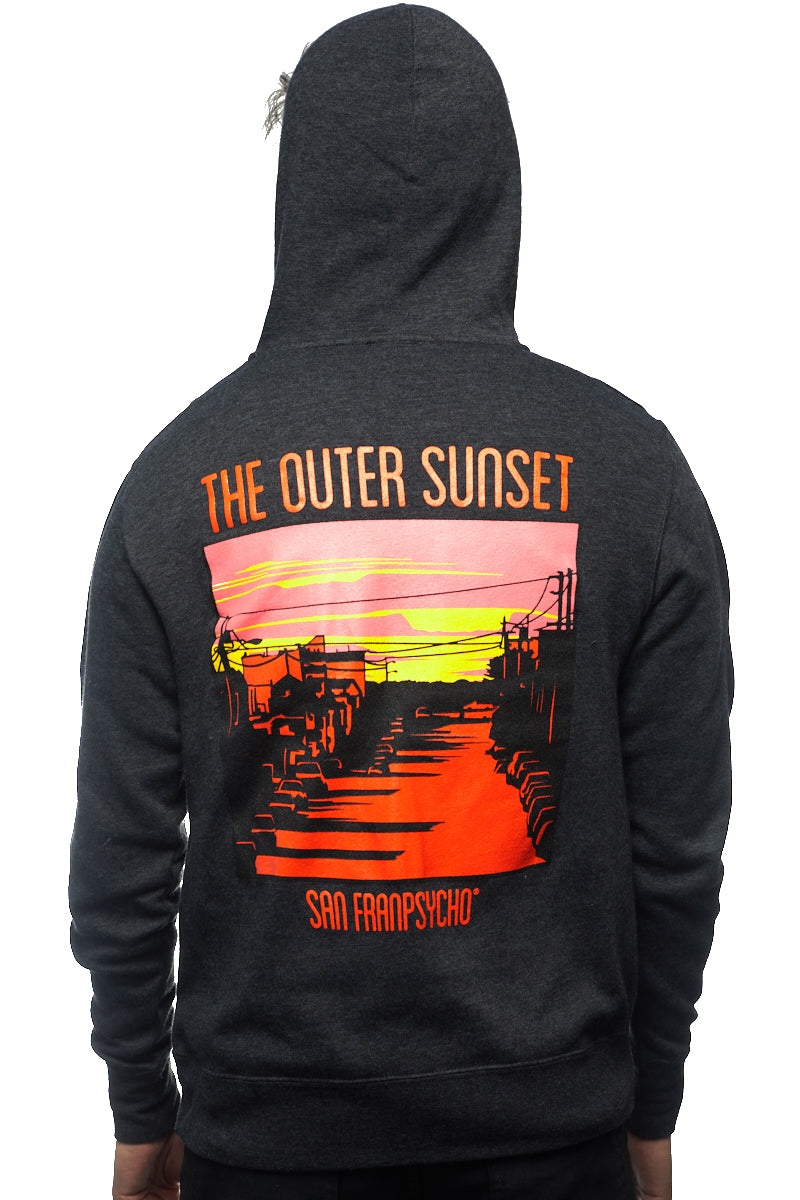 A person strolls down Noriega St, sporting an Outer Sunset Zip-Up Hoodie featuring the words "The Outer Sunset" alongside "San Franpsycho," complemented by a vibrant sunset graphic.