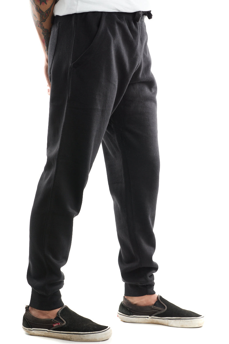 A person dressed in Black & Orange Embroidered Logo Joggers paired with comfy black slip-on shoes featuring crisp white soles.