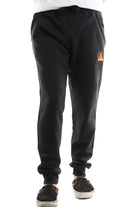 A person donning the Black & Orange Embroidered Logo Joggers, with a small orange emblem near the pocket, paired with comfortable black slip-on shoes, embodies casual elegance.