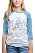 A cheerful girl is captured smiling at the camera, wearing a Youth Seal Logo Baseball Tee in blue and white, crafted from 100% cotton and featuring a charming bridge design that's perfect for kids.
