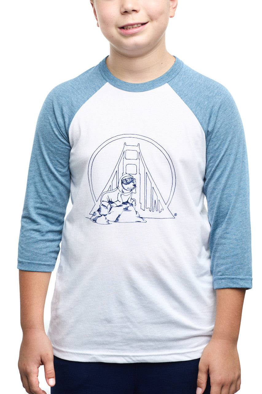The joyful child is sporting a Youth Seal Logo Baseball Tee, made from 100% cotton. This blue and white raglan shirt showcases an adorable bridge and animal design, making it ideal for kids.