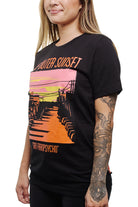 A person shows off their tattooed arm while wearing a black Outer Sunset Tee from San Franpsycho, featuring a vibrant graphic design.