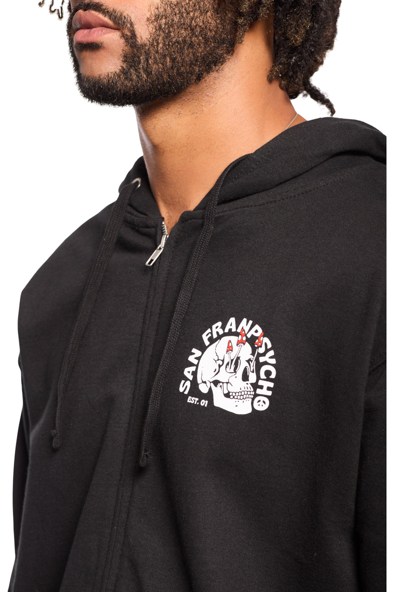The individual is wearing a black Shroom Skull Zip-Up Hoodie from San Franpsycho, adorned with a graphic logo on the chest. Made entirely of 100% cotton, this piece provides premium comfort and style, highlighting the brand's distinctive hand-printed design.