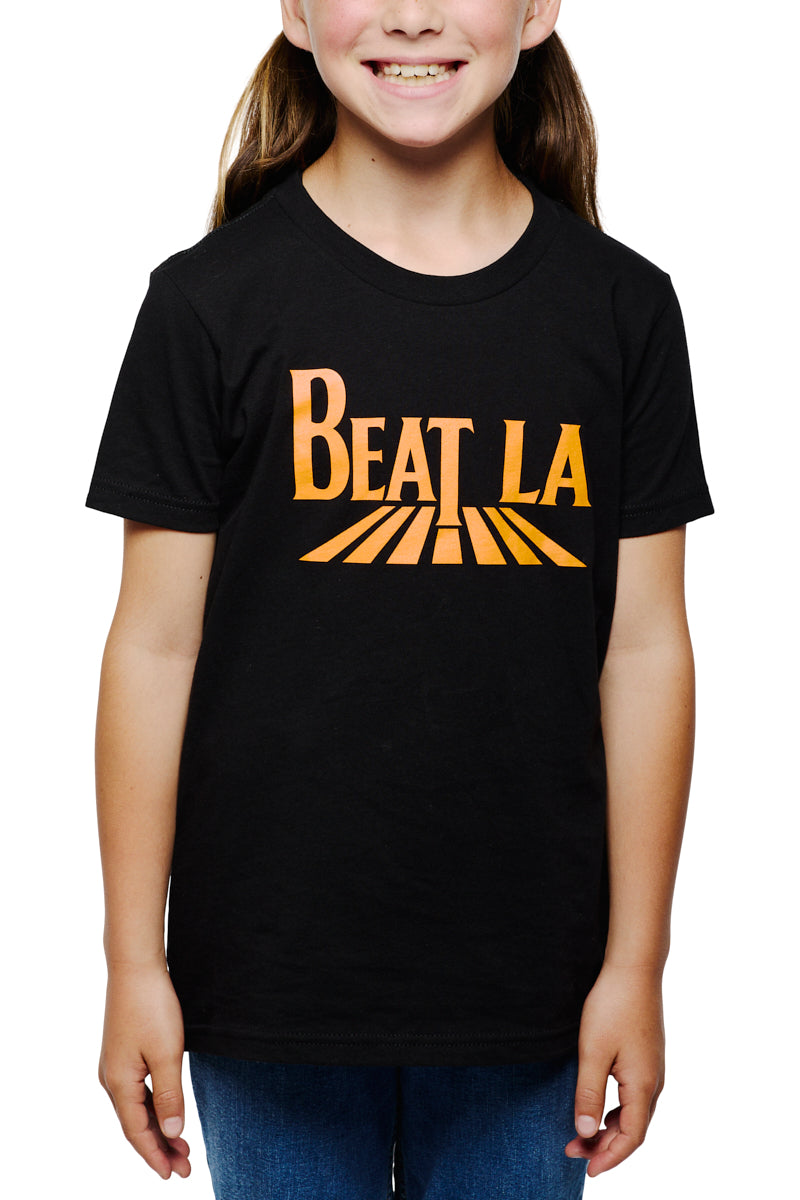 Smiling child wearing the Youth Beat LA Tee - Black & Orange, featuring bold orange lettering and a road graphic—perfect for young Bay Area sports fans—paired with classic blue jeans.