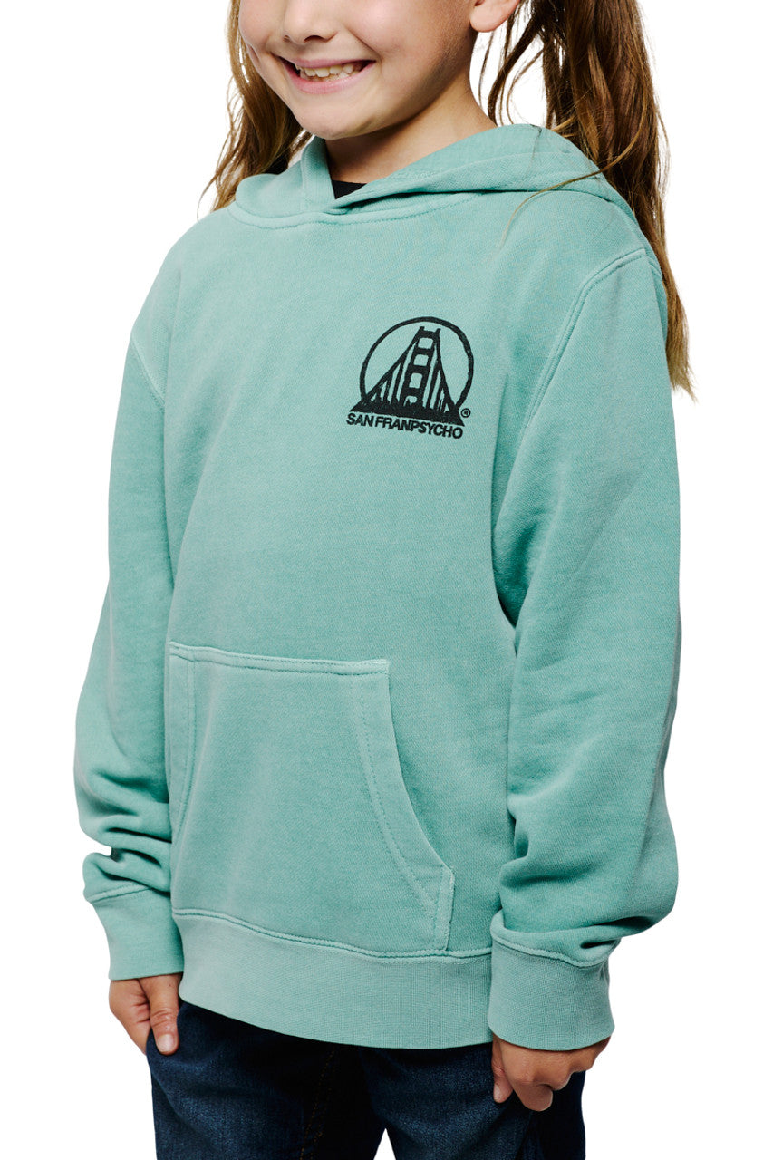 A young girl beams confidently in a light blue Youth Mint Scribble Logo Pullover Hoodie, featuring a hand-printed San Francisco scribble logo, her hands tucked comfortably into the pockets.