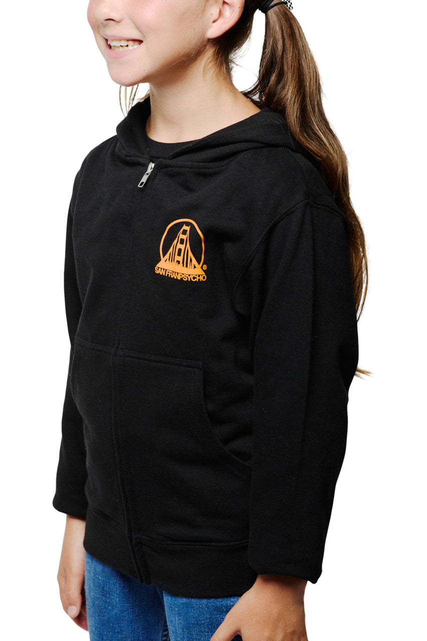 A girl wearing the Youth Black & Orange Logo Zip-Up Hoodie proudly displays the iconic San Francisco bridge logo, standing against a crisp white background.