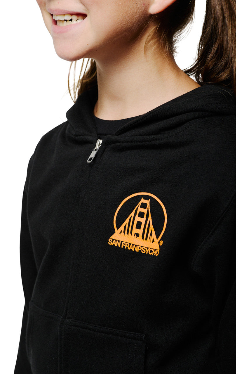 A smiling girl wearing the Youth Black & Orange Logo Zip-Up Hoodie, adorned with a golden bridge logo and San Franspycho text, made from 100% cotton.