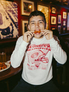 A person enjoys chicken wings in a restaurant while wearing the Candlestick Champs Crewneck, a white graphic vintage sweatshirt that captures the spirit of the Niners season.