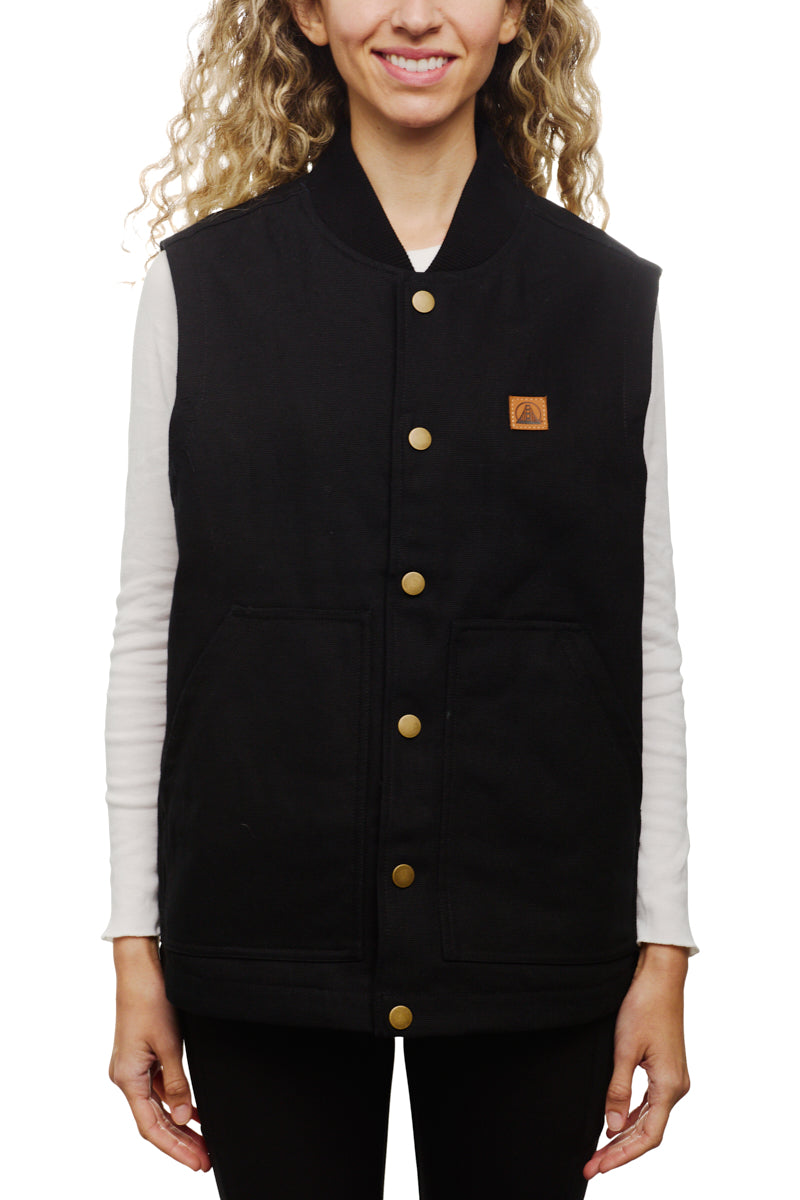 A smiling person wears the sleek Leather Patch Workwear Vest, detailed with gold buttons and front pockets, over a white long-sleeve shirt. Crafted from 100% cotton, this black sleeveless jacket blends style with functionality. Refer to the size guide for the perfect fit.