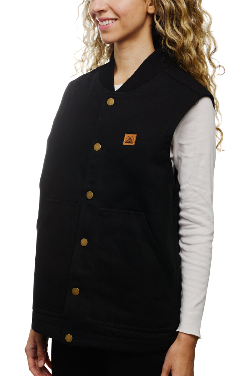 A person is smiling while wearing a Leather Patch Workwear Vest, featuring a black button-up design crafted from 100% cotton, layered over a white long-sleeve shirt for a blend of classic style and comfort.