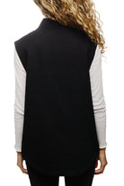 A woman with curly hair is seen from the back, wearing the Leather Patch Workwear Vest over a white long-sleeve shirt, crafted from 100% cotton for that perfect fit.