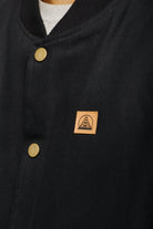 Close-up of the Leather Patch Workwear Vest in black, featuring gold buttons and a small brown square patch adorned with a bridge design, reflecting the rugged style akin to canvas workwear vests.