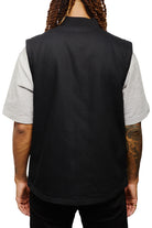 A person with long hair is seen from the back, wearing a Leather Patch Workwear Vest over a gray shirt.