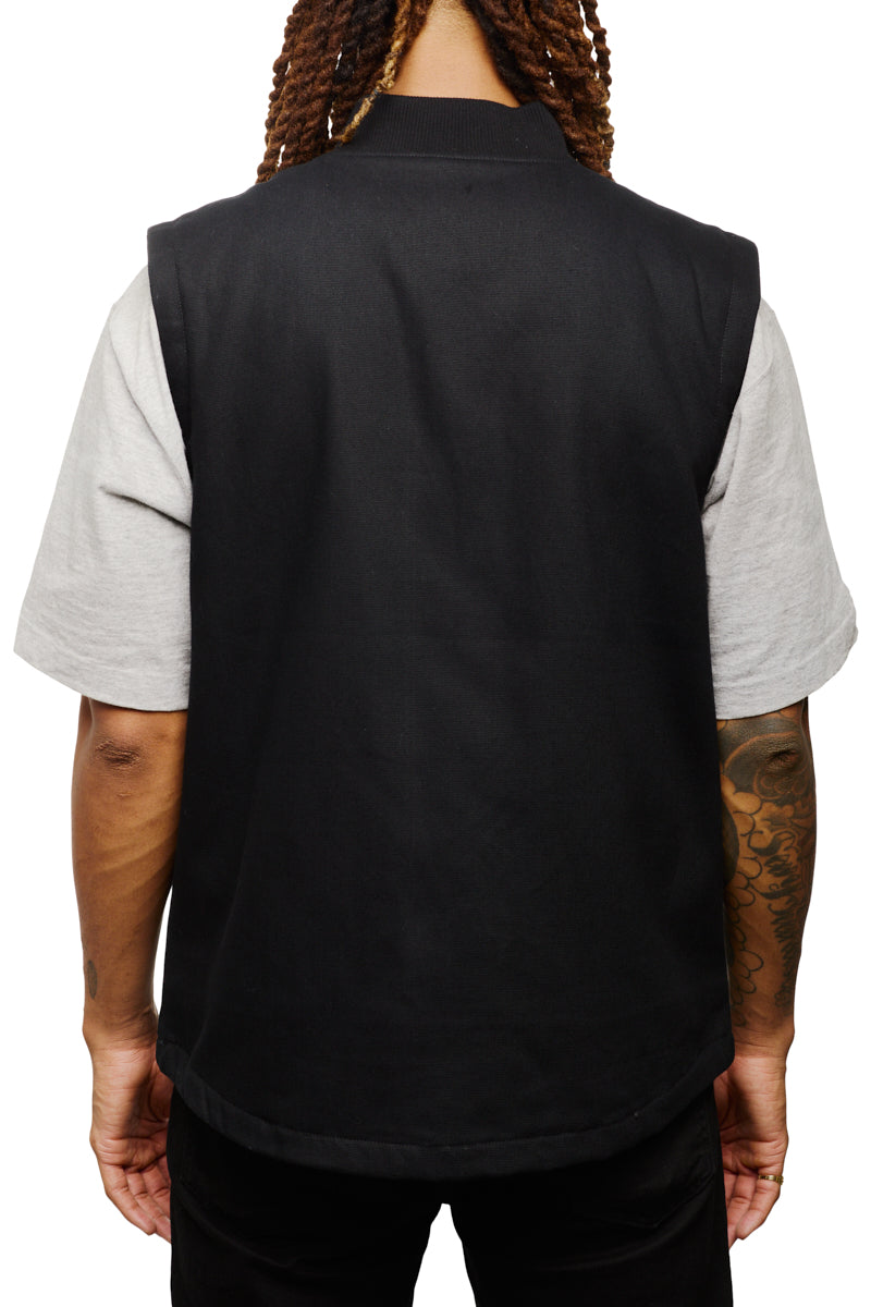 A person with long hair is seen from the back, wearing a Leather Patch Workwear Vest over a gray shirt.
