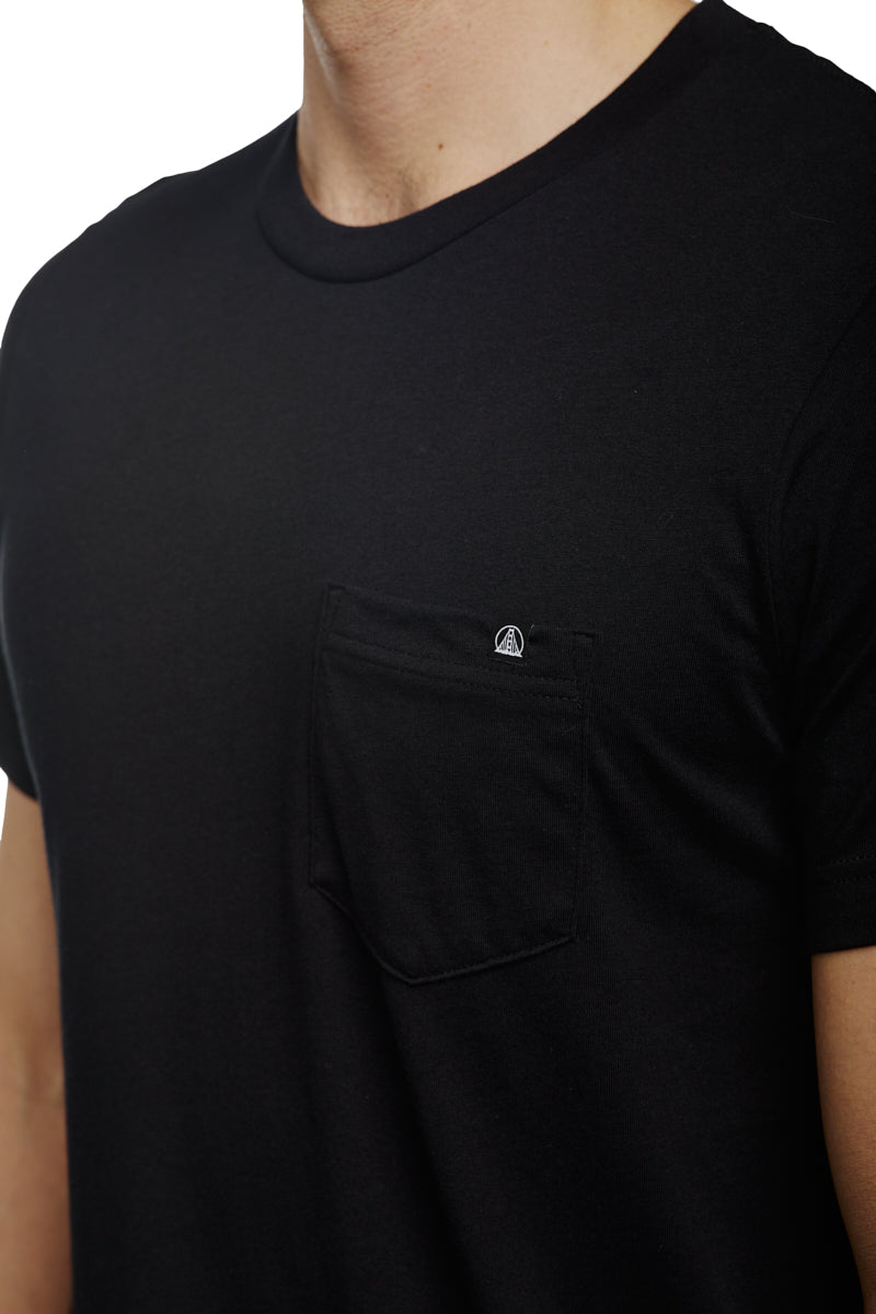 The individual is wearing the Black Pocket Tee w/ SFP Clip Label, expertly crafted from soft Airlume cotton and featuring a small pocket on the left chest.