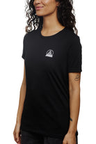 An individual wearing a Women's Mini Logo Tee in black, displaying a white bridge graphic, with arms at their sides against a white background.