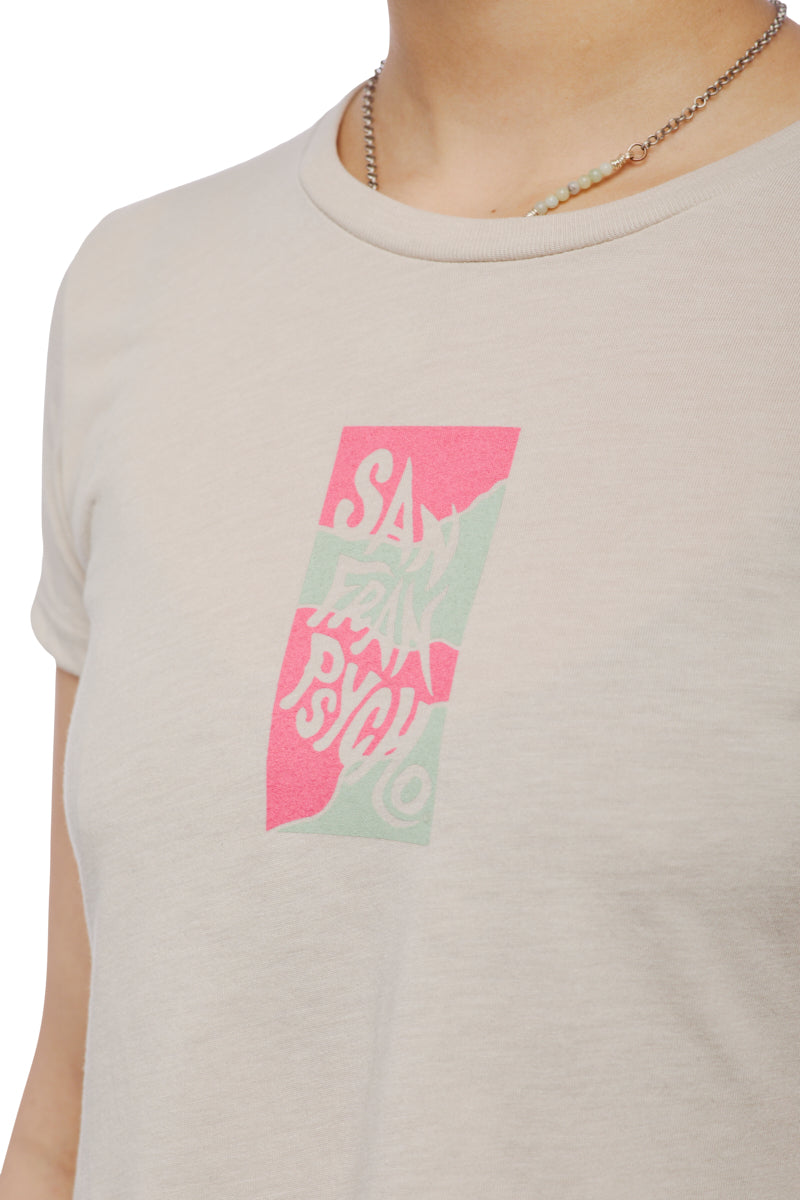 A person wearing the Trippy Psycho Crop Top, a beige T-shirt with a pink and green San Francisco graphic from the Spring 2023 Collection, paired with a small beaded necklace.