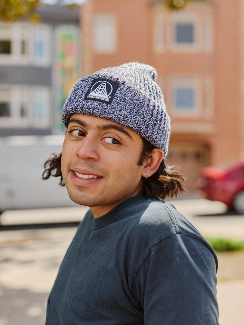 Person wearing a Zebra Lumberjack Beanie with Black/White SFP Logo and a dark shirt, looking over their shoulder outdoors in a city setting.