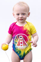 A pink and yellow hand-printed Tie-Dye Onesie featuring a Golden Gate Bridge graphic.