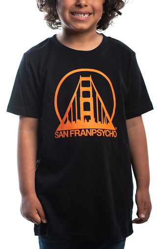 A child smiles brightly, wearing the Youth Black & Orange Logo Tee that showcases an orange bridge logo and the iconic San Franpsycho text, capturing the vibrant spirit of San Francisco.